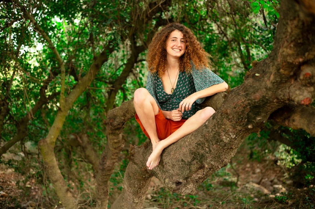 קארין יושבת על ענף של עץ ביער ומחייכת
